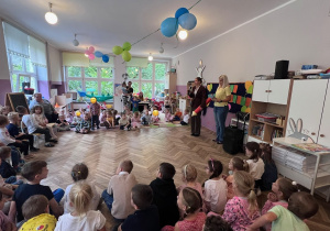 Dzieci z całego przedszkola siedzą na dywanie i słuchają przywitania wygłaszanego przez panią dyrektor
