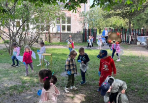 Dzieci spacerują po ogrodzie i zbierają śmieci do worków
