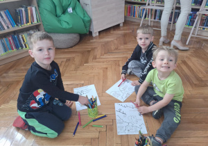 Chłopcy siedzą na podłodze i kolorują kredkami fragmenty mapy Polski