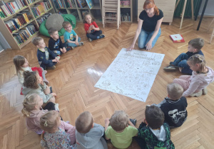 Przedszkolaki siedzą w kole i oglądają dużą mapę Polski w formie kolorowanki