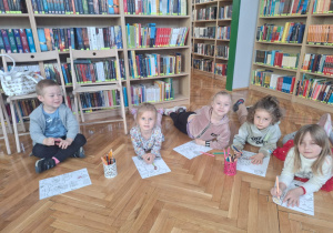 Dzieci siedzą i malują kredkami fragmenty mapy Polski