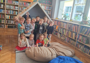Dzieci siedzą na wielkich poduchach, w tle widać regały z książkami