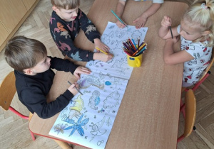 Chłopcy kolorują wspólnie dużą kolorowankę przy stoliku