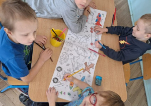 Chłopcy siedzą przy stoliku i malują wielkoformaowy obrazek