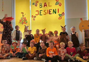 Zdjęcie grupowe na tle napisu bal jesieni dzieci z grupy 4 razem z panią muzyczką