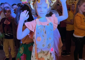 Dziewczynka z grupy 5 tańczy w jesiennym przebraniu wśród kolorowych świateł