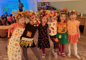 Dziewczynki z grupy 5 w jesiennych przebraniach stoją uśmiechnięte