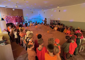 Zabawa taneczna z pomarańczowym materiałem rozciągniętym pomiędzy dziećmi, na materiale podskakują balony