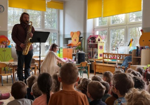 Dzieci oglądają i słuchają jak pan gra na saksofonie
