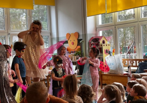 Wybrane dzieci w strojach karnawałowych tańczą a prowadząca śpiewa