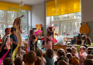 Wybrane dzieci w strojach karnawałowych tańczą a prowadząca śpiewa i macha ręką