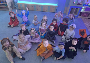 Dzieci z grupy 3 w przebraniach, siedzą na dywanie i uśmiechają się