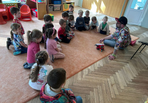 Dzieci z grupy 2 siedzą na dywnie i rozmawijają z panem Markiem
