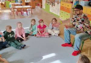Dzieci z grupy 4 siedzą na dywnie i rozmawijają z panem Markiem