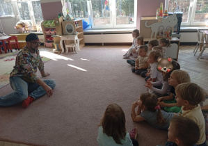 Dzieci z grupy 1 siedzą na dywnie i rozmawijają z panem Markiem