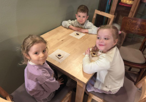 Dwie dziewczynki i chłopiec siedzą przy stoliku podczas poczęstunku