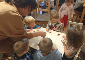 Pani z Baśniowej Kawiarenki rozdaje dzieciom z grupy 1, siedzącym przy stoliku, poczęstunek