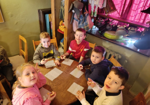 Chłopcy i dziewczynka z grupy 5 siedzą przy stoliku podczas poczęstunku