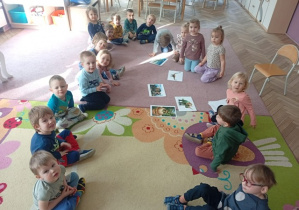 Dzieci siedzą w kole i oglądają ilustracje dinozaurów