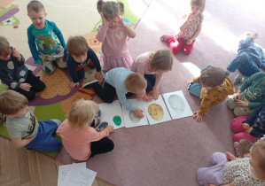 Dzieci siedzą na dywanie i układają zdjecia z jajami dinozurów