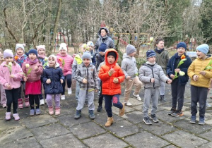 Dzieci z grupy 4 i 5 trzymają w dłoniach instrumenty i tulipany, stoją na tarasie