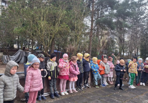 Dzieci z grupy 3 stoją na tarsie, śpiewają i grają na tamburynach