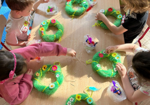 Dzieci z gr 2 siedzą przy stoliku i naklejają ozdoby