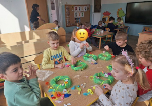 Przedszkolaki z gr 3 siezą przy stoliku i dekorują swoje wianki wielkanocne