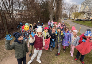 Uśmiechnięte dzieci z gr 3 i 4 z workami w rękach sprzątają bliską okolice przedszkola