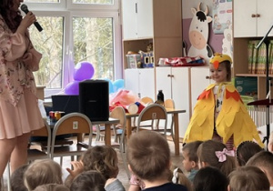 Prowadząca śpiewa piosenkę, dziewczyna z gr 1 stoi obok w stroju kurki