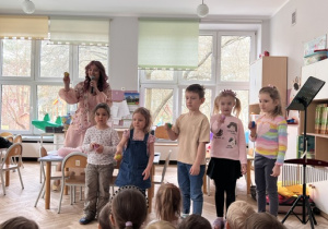 Dzieci po jednym z każdej grupy stoją na środku sali i grają na grzechotkach