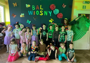 Zdjęcie grupowe grupy 5 z panią muzyczką, na tle kolorowej dekoracji wiosennej