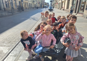 Dzieci z grupy 3 siedzą na ławeczce przy ulicy Piotrkowskiej