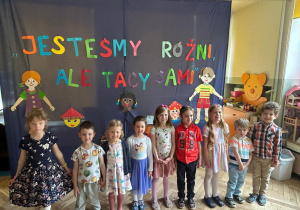Zdjęcie uczestników konkursu stojących na tle kolorowej dekoracji z napisem Jesteśmy różni, ale tacy sami