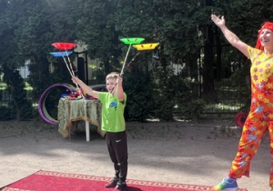 Chłopiec z 1 grupy stoi na scenie i trzyma trzy kijki, na których wirują 3 dyski