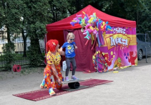 Dziewczynka z 2 grupy w niebieskiej bluzie stoi na równoważni z panią z cyrku