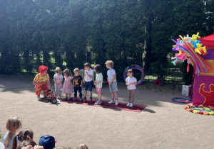 Dzieci z różnych grup stoją na scenie. Pani trzyma mini rowerek i pokazuje dzieciom
