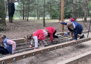 Dzieci przechodzą przez sznurkową siatkę zawieszoną nad ziemią
