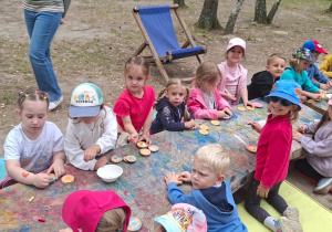 Przedszkolaki z 2 grupy siedzą przy drewnianych stołach podczas warsztatów malowania pastelami drewnianych kółek