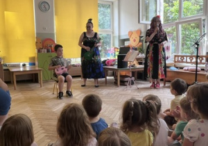 Chłopiec z grupy 5 siedzi na krzesełku na scenie i gra na ukulele