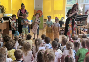 Chłopcy z gitarami i dziewczynki w strojach hawajskich tańczą i grają na scenie