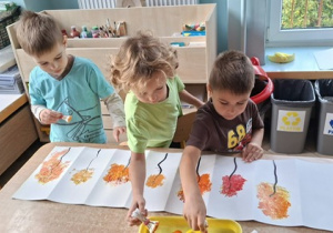 Chłopcy z grupy 3 malują farbami listki na jesiennych drzewach na kartonie
