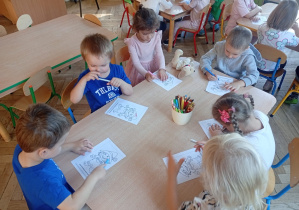 Dzieci siedzą przy stoliku i kredkami kolorują postać z kumpelkowa